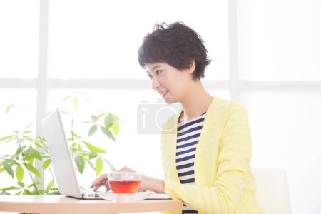 Téléchargez les photos : Jeune femme travaillant sur ordinateur portable avec du thé - en image libre de droit