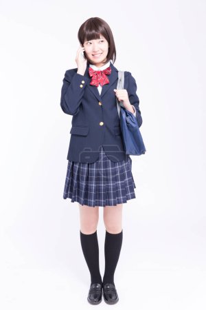 Photo for Studio portrait of smiling Japanese schoolgirl talking on smartphone - Royalty Free Image