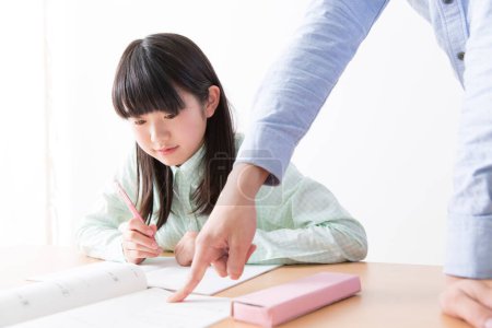 Photo for Cute Asian girl doing homework with father at home - Royalty Free Image