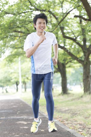 Photo for Sporty Japanese man jogging in summer park - Royalty Free Image
