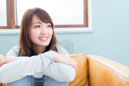 Téléchargez les photos : Femme assise sur le canapé et souriante - en image libre de droit