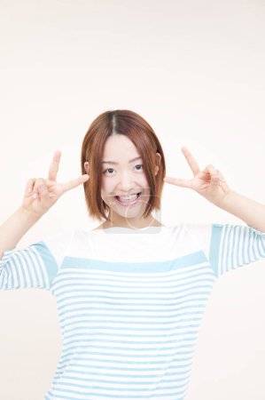 Porträt der schönen jungen Japanerin mit V-Zeichen auf beigem Hintergrund