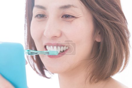 Foto de Retrato de hermosa mujer japonesa madura cepillarse los dientes sobre fondo blanco - Imagen libre de derechos