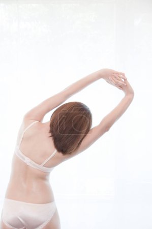 Foto de Vista trasera de mujer joven en lencería blanca que se extiende delante de la ventana - Imagen libre de derechos
