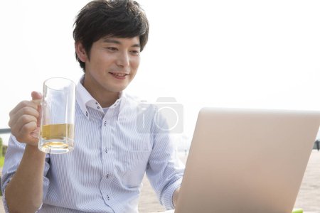 Foto de Joven asiático hombre bebiendo cerveza y trabajando en portátil en la playa - Imagen libre de derechos