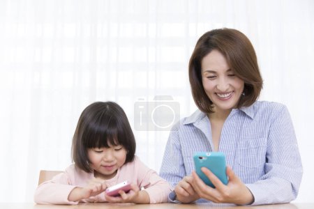 Téléchargez les photos : Sourire asiatique mère et fille à l'aide de téléphones - en image libre de droit