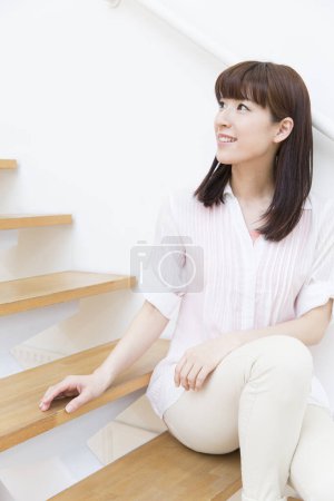 Téléchargez les photos : Portrait de jeune femme souriante assise dans les escaliers à la maison - en image libre de droit