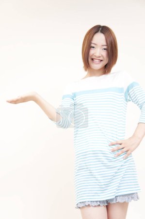 Téléchargez les photos : Portrait de belle jeune femme japonaise pointant vers l'espace vide sur fond beige - en image libre de droit