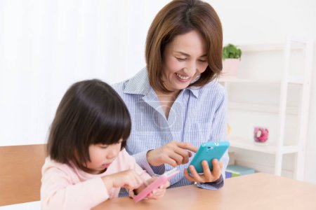 Photo for Smiling asian mother and daughter using phones - Royalty Free Image