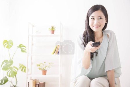 Téléchargez les photos : Asiatique femme à l'aide de télécommande et sourire - en image libre de droit
