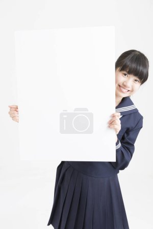 Foto de Retrato de hermosa joven estudiante en uniforme escolar sosteniendo cartel en blanco sobre fondo blanco - Imagen libre de derechos