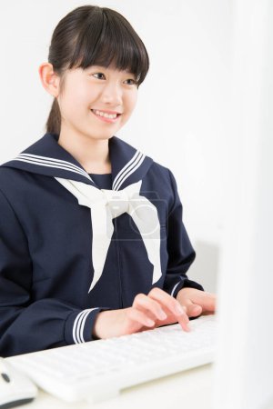 Téléchargez les photos : Portrait de belle jeune étudiante en uniforme scolaire étudiant avec ordinateur - en image libre de droit