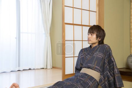 Téléchargez les photos : Portrait de beau jeune homme japonais en yukata traditionnel dans un hôtel de source chaude ethnique - en image libre de droit