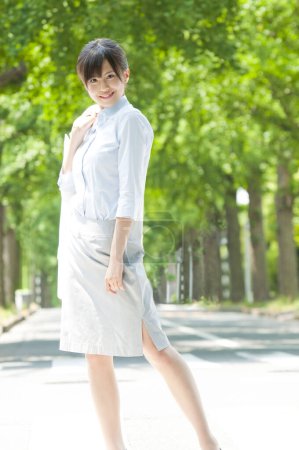 Téléchargez les photos : Portrait extérieur d'une femme japonaise joyeuse marchant dans un parc d'été verdoyant - en image libre de droit