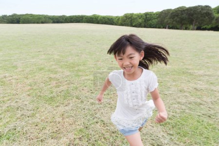 Foto de Linda chica japonesa caminando en el parque de verano, retrato diurno de un niño divertido divirtiéndose al aire libre - Imagen libre de derechos