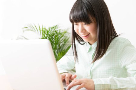 Téléchargez les photos : Souriant japonais fille assis à la table avec ordinateur portable - en image libre de droit