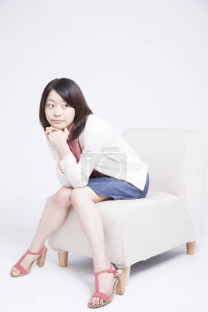 Téléchargez les photos : Portrait de belle jeune femme japonaise sur chaise sur fond clair - en image libre de droit