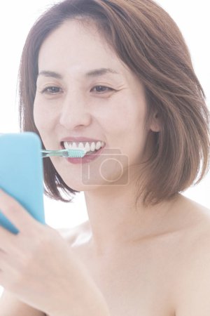 Photo for Portrait of beautiful mature japanese woman brushing teeth on white background - Royalty Free Image
