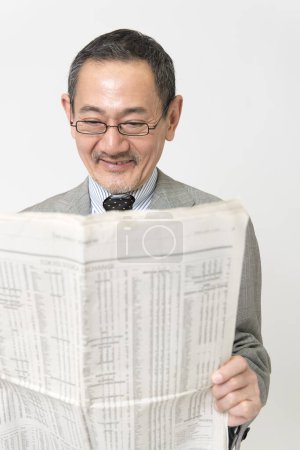 Téléchargez les photos : Portrait de mature asiatique homme d'affaires lecture journal sur fond blanc - en image libre de droit