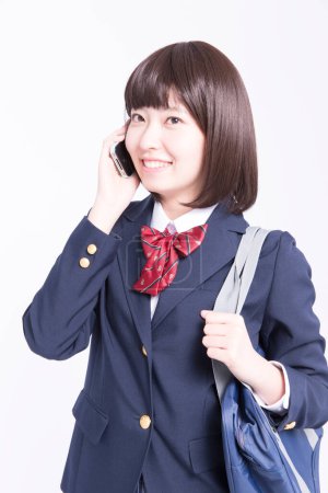 Photo for Studio portrait of smiling Japanese schoolgirl talking on smartphone - Royalty Free Image
