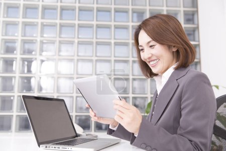 Téléchargez les photos : Femme d'affaires japonaise en costume en utilisant une tablette au bureau - en image libre de droit
