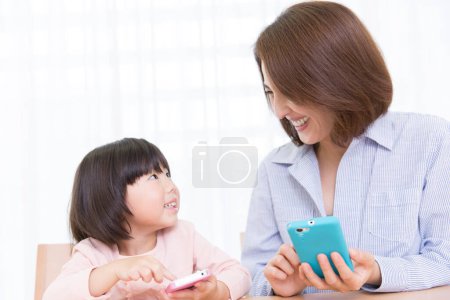Foto de Sonriente asiático madre y hija usando teléfonos - Imagen libre de derechos