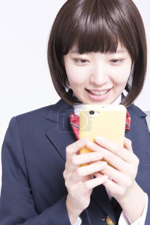Foto de Retrato de estudio de una colegiala japonesa sonriente usando un teléfono inteligente - Imagen libre de derechos