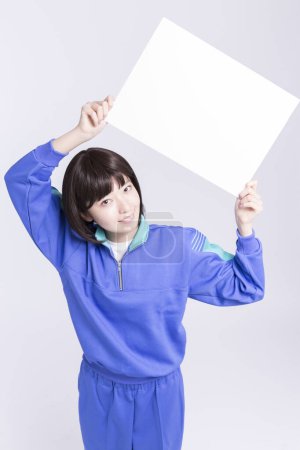 Foto de Joven asiático mujer usando azul chándal celebración vacío en blanco tablero sobre blanco fondo - Imagen libre de derechos