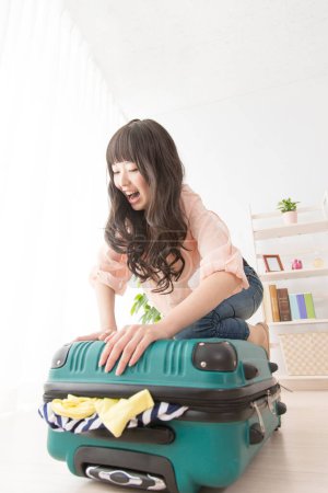 Photo for Happy young asian woman packing her suitcase - Royalty Free Image
