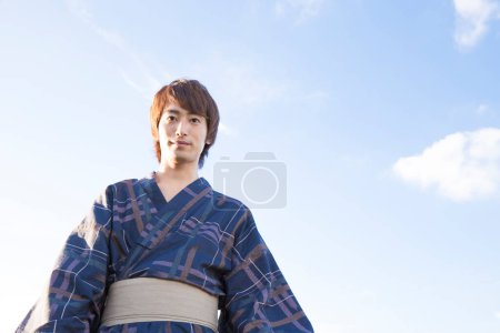 Photo for Bottom view portrait of handsome japanese young man in traditional yukata on blue sky background - Royalty Free Image
