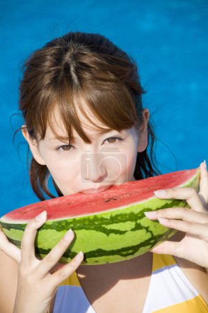 Téléchargez les photos : Jeune femme japonaise en maillot de bain coloré mangeant pastèque près de la piscine - en image libre de droit