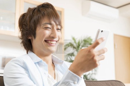 Téléchargez les photos : Jeune asiatique gars en utilisant smartphone à la maison. - en image libre de droit