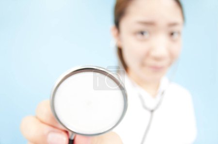 Téléchargez les photos : Portrait grand angle de belle jeune infirmière japonaise avec stéthoscope en uniforme sur fond bleu - en image libre de droit
