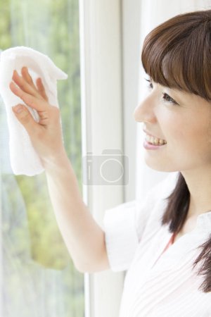 Téléchargez les photos : Jeune femme nettoyage fenêtre à la maison - en image libre de droit