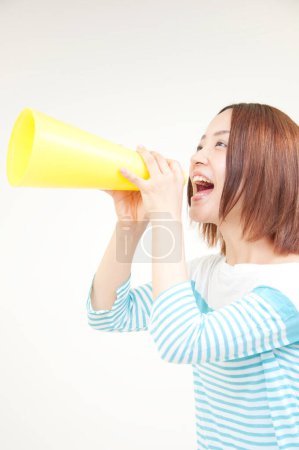 Téléchargez les photos : Portrait de belle jeune femme japonaise criant avec haut-parleur sur fond beige - en image libre de droit