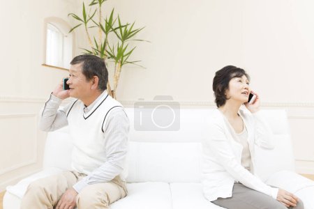 Photo for Asian couple on sofa with phones - Royalty Free Image