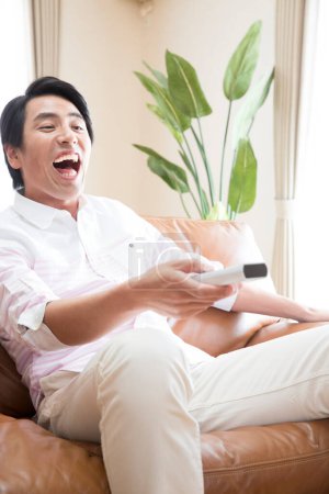 Téléchargez les photos : Asiatique homme regarder la télévision à la maison - en image libre de droit