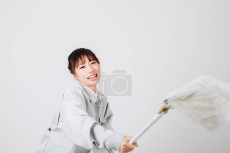 Téléchargez les photos : Asiatique femme nettoyage l 'plancher sur un gris fond - en image libre de droit