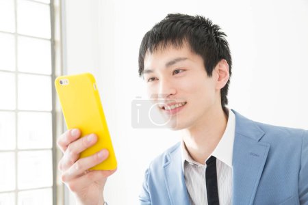 Téléchargez les photos : Portrait en gros plan d'un jeune homme d'affaires japonais utilisant un smartphone - en image libre de droit