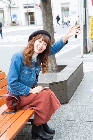 Photo for Young woman sitting on the bench  waving hand in the city - Royalty Free Image