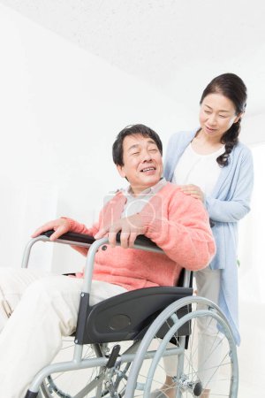 Foto de Mujer ayudando a hombre en silla de ruedas en casa - Imagen libre de derechos