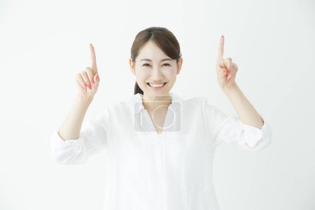 Téléchargez les photos : Belle femme d'affaires japonaise pointant vers le haut avec les doigts sur fond blanc - en image libre de droit