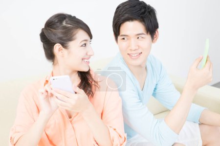 Téléchargez les photos : Couple utilisant des smartphones à la maison - en image libre de droit