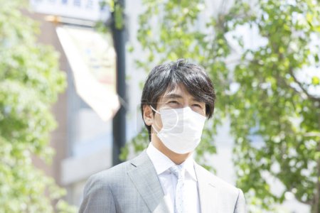 Téléchargez les photos : Beau professionnel japonais homme d'affaires en masque visage sur la rue - en image libre de droit