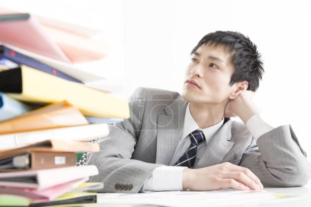 Photo for Close-up portrait of young japanese businessman looking at pile of paperwork at office - Royalty Free Image