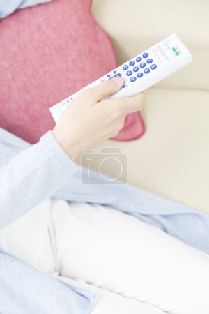 Téléchargez les photos : Femme tenant la télécommande sur le canapé - en image libre de droit