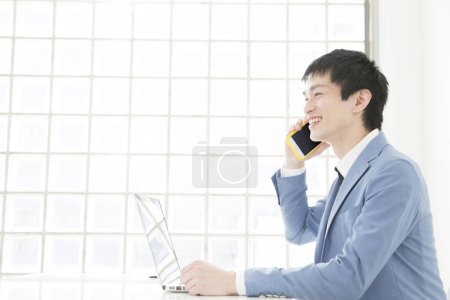 Photo for Close-up portrait of young japanese businessman talking by phone at office - Royalty Free Image
