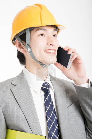 Téléchargez les photos : Portrait en gros plan de jeune homme d'affaires japonais avec chapeau dur parlant par téléphone - en image libre de droit