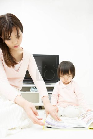 Photo for Young asian mother and cute daughter reading book at home - Royalty Free Image