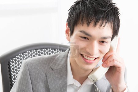 Téléchargez les photos : Portrait en gros plan d'un jeune homme d'affaires japonais parlant par téléphone au bureau - en image libre de droit